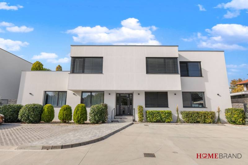 A building with a minimalist design, greenery, and a parking lot on Lipnicka Street in Dunajska Luzna.