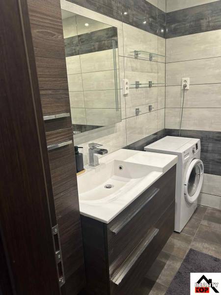 A bathroom in a 3-room apartment with a sink, washing machine, and mirrored wall.