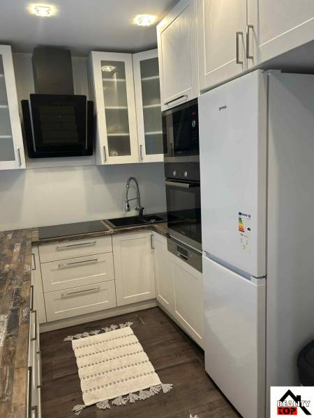 A kitchen in a 3-room apartment with white cabinets and a wood-patterned floor.