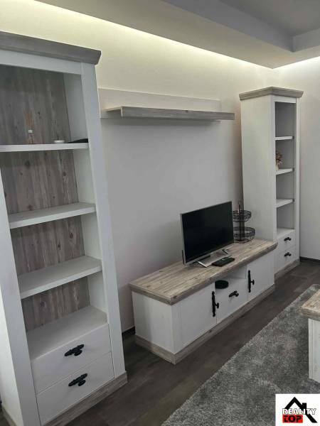 Living room in a 3-room apartment with shelves, a television, and a wooden decor floor.