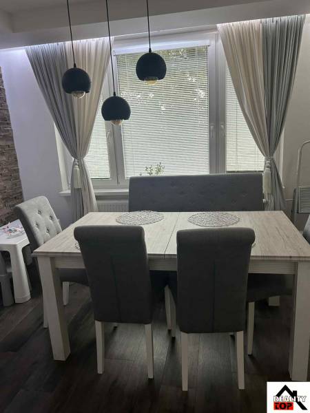 Dining area in a 3-room apartment with dark flooring and curtains, gray furniture.