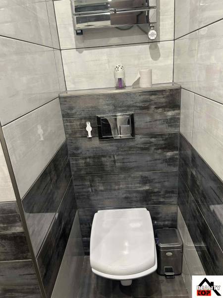 Toilet in a 3-room apartment with dark tiles and a wall-mounted towel holder.