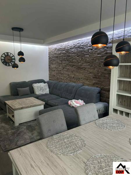 Living room with a corner sofa, hanging lamps, and decorative stone cladding in a 3-room apartment.