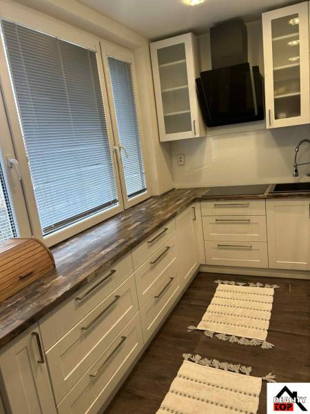 A kitchen in a 3-room apartment with a wooden decor floor and light cabinets.