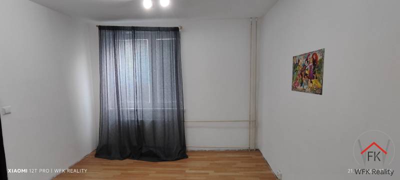 A room with a wooden decor floor and a painting in a three-room apartment, curtains on the windows.