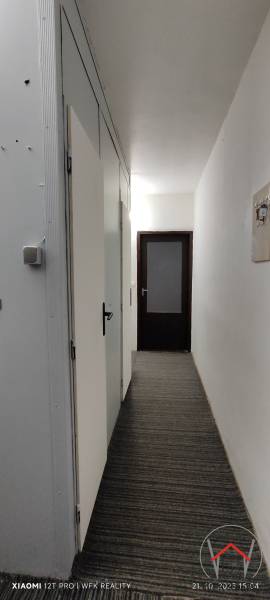 A narrow hallway in a 3-room apartment with white walls and dark doors.