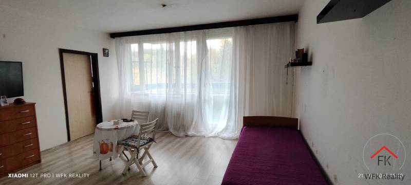 A room in a three-room apartment with a bed, table, chairs, and a floor with a wooden decor.