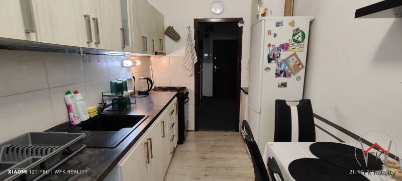 A kitchen with a wood-patterned floor, a kitchen unit, and a refrigerator in a three-room apartment.