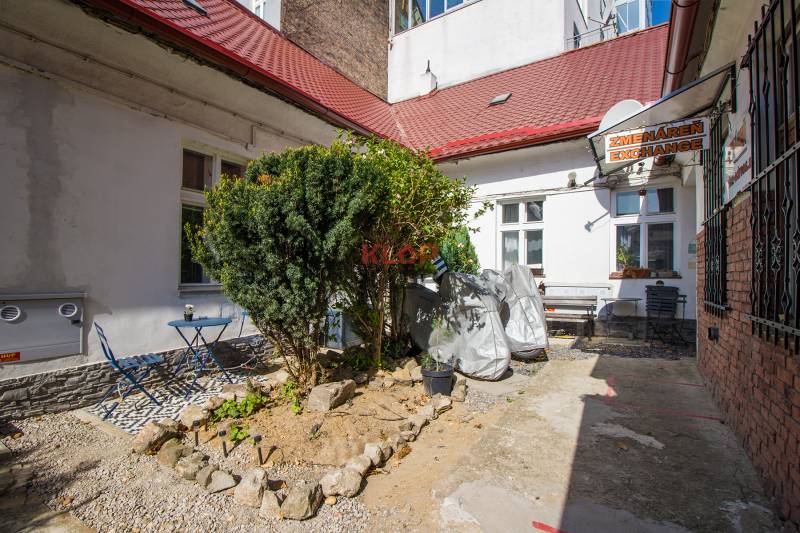A garden in Bratislava on Obchodná Street with benches, a table, and a bush in front of the exchanger.