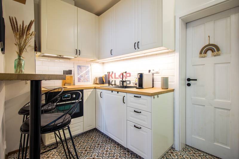 A kitchen in a studio apartment with white cabinets and patterned flooring.