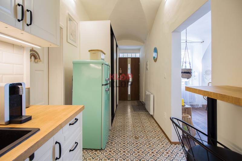 The kitchen of a one-room apartment with a mint refrigerator, a coffee maker, and a patterned floor.