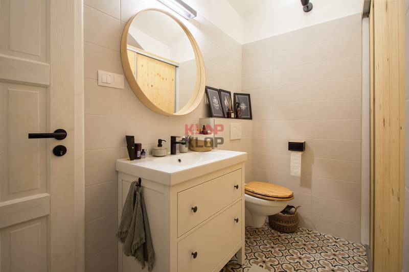 Bathroom in a studio apartment with a round mirror, patterned tiles, light-colored tiles.