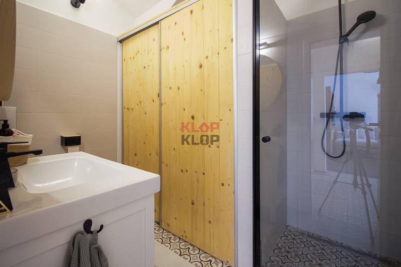 Bathroom with a glass shower enclosure, wooden doors, and light tiles in a studio apartment.