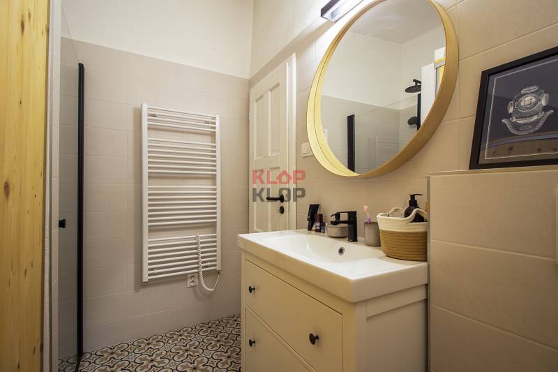 A bathroom in a studio apartment with a prominent round mirror and decorative tiles.