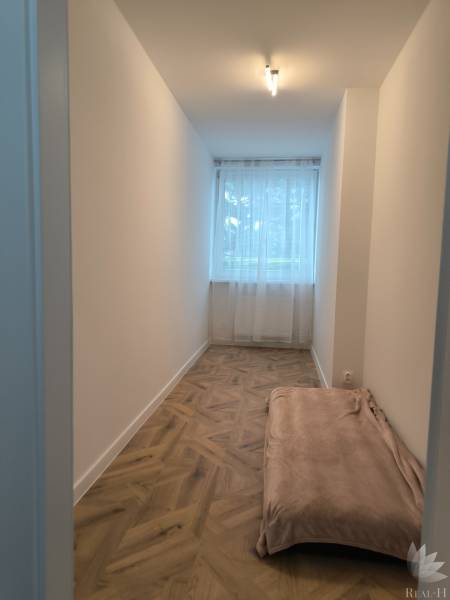 A narrow room with a light wall, a floor with a wooden decor, and a bed.