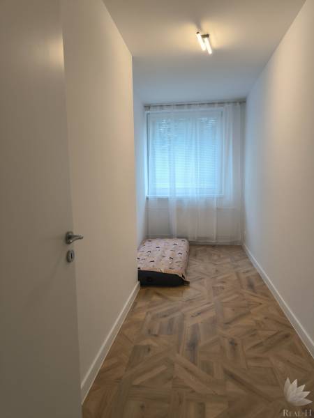 A narrow room in a 4-room apartment with a wooden decor floor and a mattress.