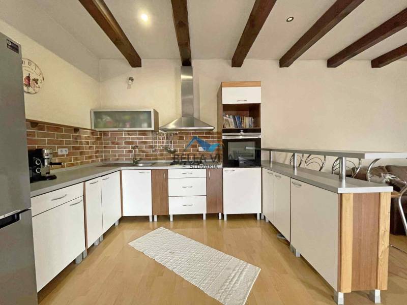 A kitchen in a family house with a wooden decor floor, light furniture, and brick cladding.