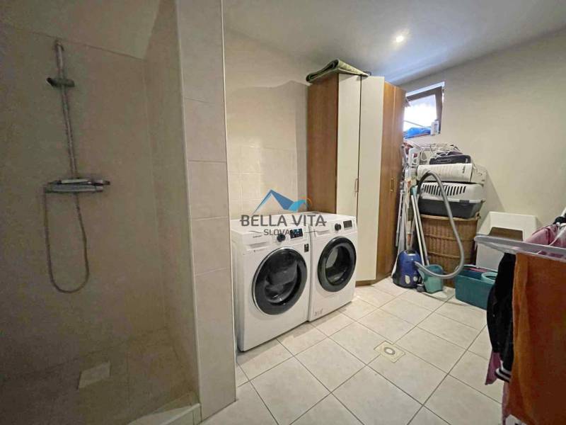 Laundry room in a family house with a washing machine, dryer, shower, and storage spaces.