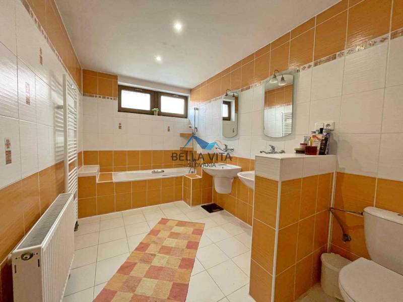 A bathroom in a family house with orange and white tiles, a bathtub, and a sink.