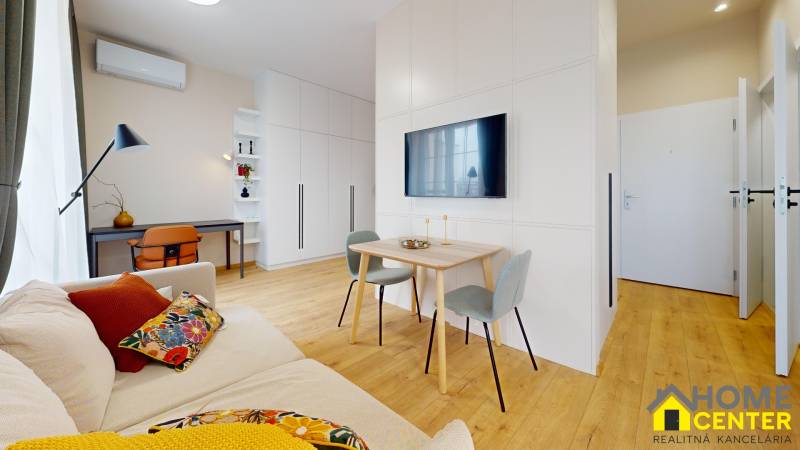 Living room in a studio apartment with wood-patterned flooring, a work corner, seating area.