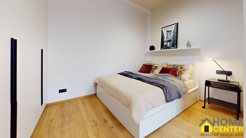 A bedroom in a studio apartment with a bed, shelf, table, and floor with a wooden decor.