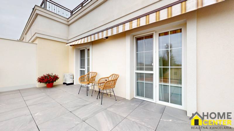 A terrace with tiles, wicker chairs, and an awning in a studio apartment in Komárno.