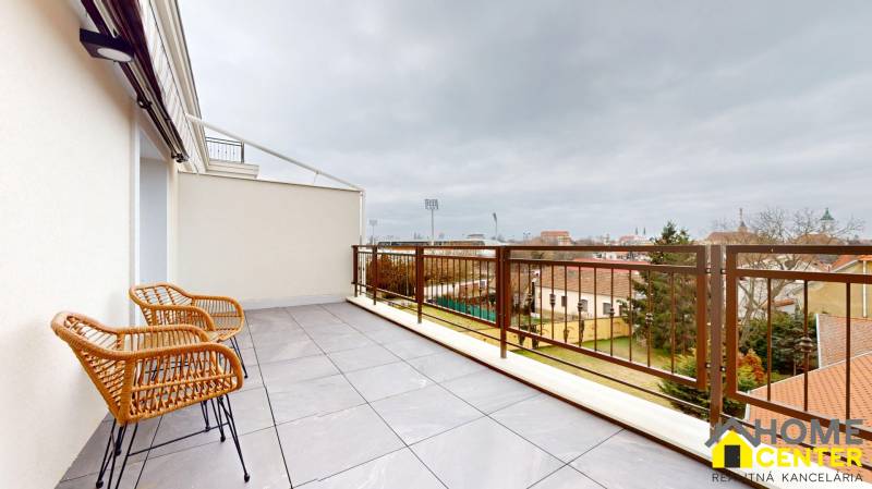 Spacious balcony in Komárno at a 1-room apartment with rattan chairs and a view of the city.