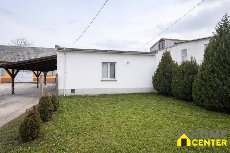 A space in Pribete with a lawn, trees, and a simple white structure for gastro use.