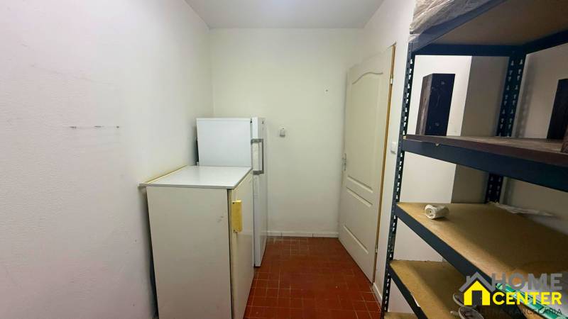 A narrow room in a catering area with refrigerators and a metal shelf.