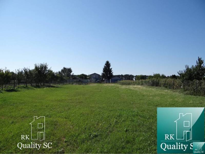 Extensive green residential plot in Jelka, Vrbová Street, bordered by trees.