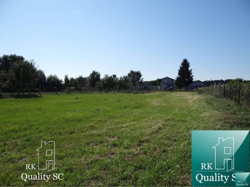 A grassy residential plot on Vrbová Street in Jelka, surrounded by trees and fencing.