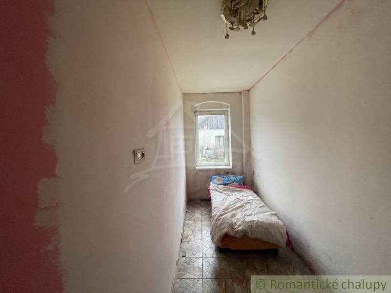 A narrow room in a family house with a bed, a window, and ceramic flooring.