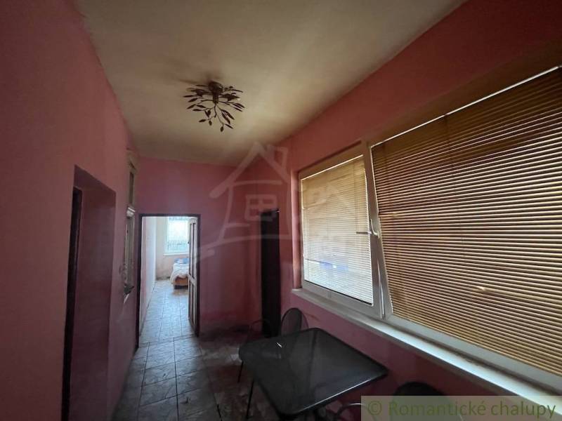 A hallway in a family house with pink walls, blinds, and a ceiling light.