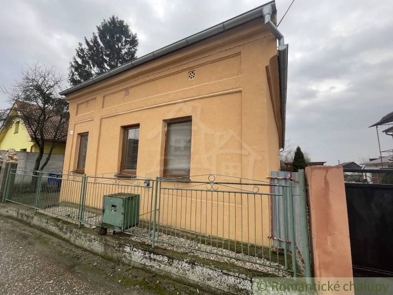 An orange family house in Neded surrounded by a fence, next to trees and other houses.