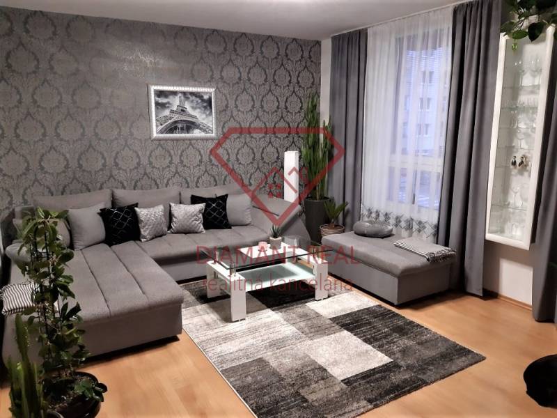 Living room with a large gray sofa, decorative wallpaper, and wood-patterned flooring.