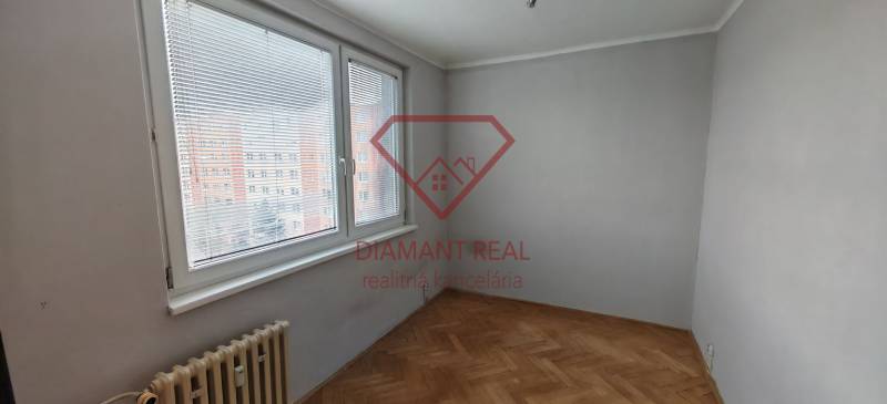 A room with a wooden decor floor and a large window in a 3-room apartment.