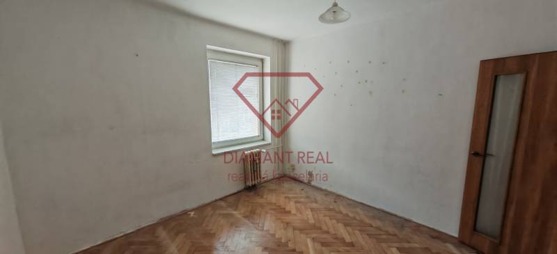 A room in a 3-room apartment with a wooden decor floor, white walls, a window, a radiator.