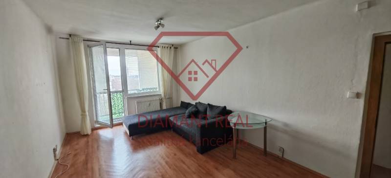 Living room in a three-room apartment with a wooden decor floor and a view through a large window.