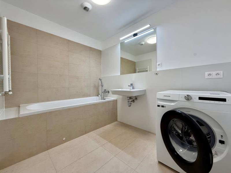 Bathroom in a 3-room apartment with a bathtub, washing machine, and sink, bright tiles.
