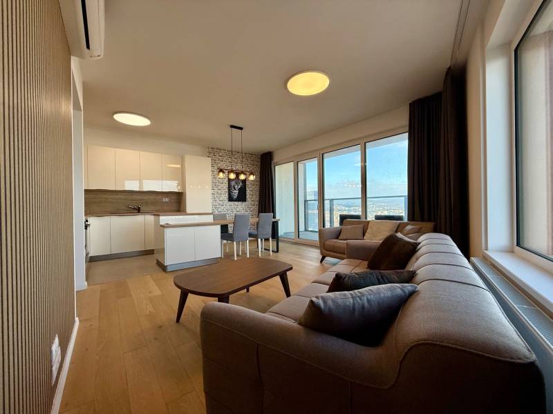 Living room with a kitchen in a three-room apartment, with a wooden decor floor and large windows.