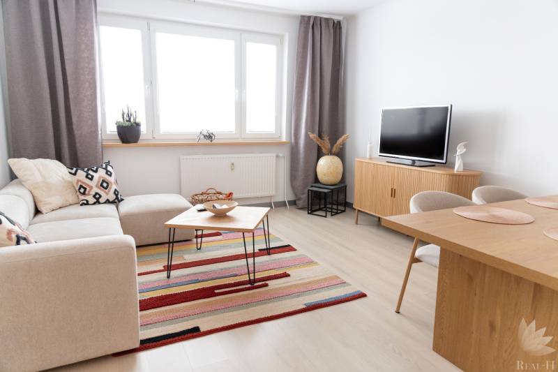 Living room in a 4-room apartment with a wooden decor floor, a sofa, and a television.