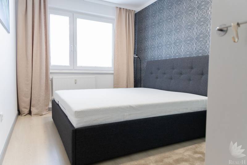 Bedroom in a 4-room apartment with a bed, wallpaper, windows, and curtains, floor with wooden decor.