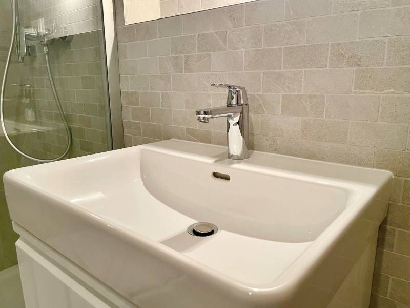 Bathroom in a 2-room apartment with a sink and a shower stall with glossy tiles.