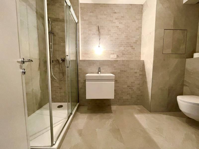 A bathroom in a 2-room apartment with stone tiles and a shower corner.