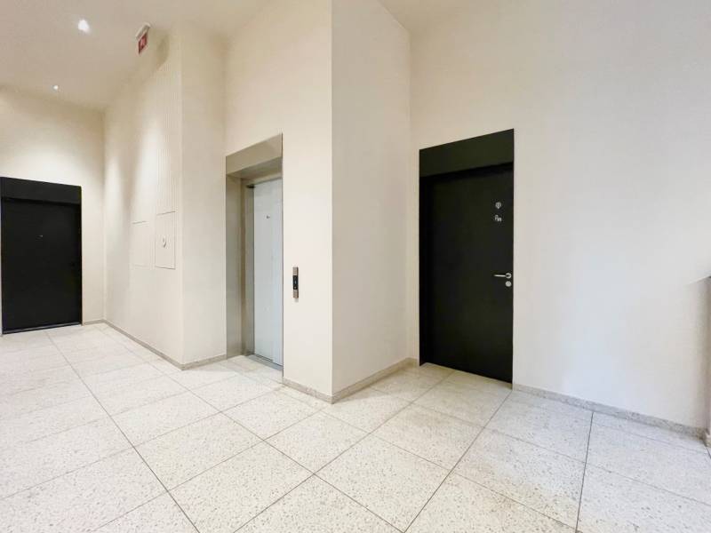 A hallway with an elevator and two black doors in a 2-room apartment.