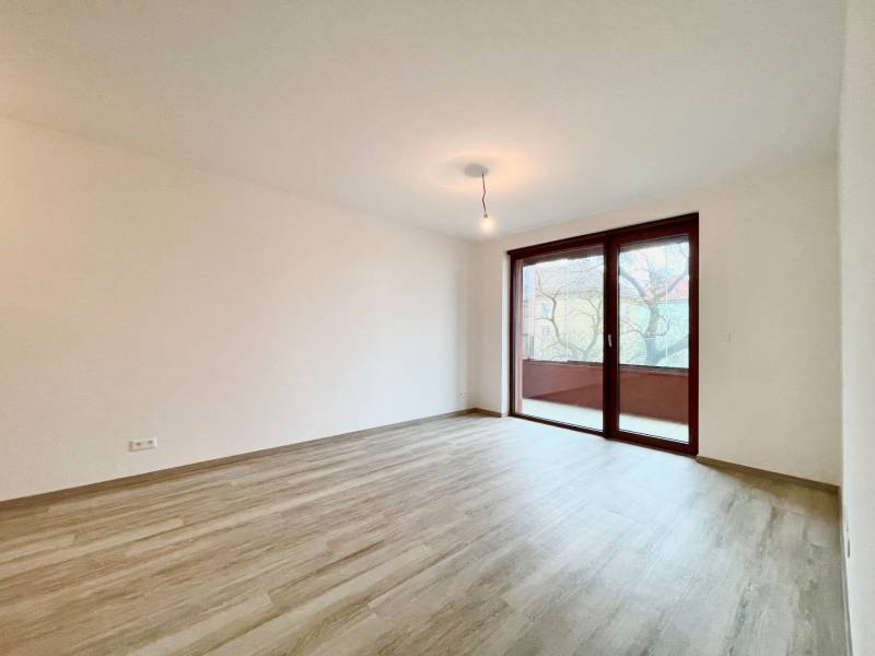 A spacious room with a large window and a wooden decor floor in a 2-room apartment.