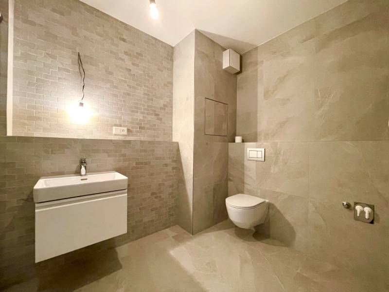 Bathroom with a wall-mounted toilet and sink in a two-room apartment with neutral tiles.