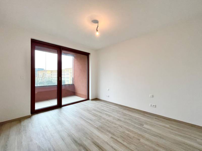 A room in a 2-room apartment with a wooden decor floor and a balcony.