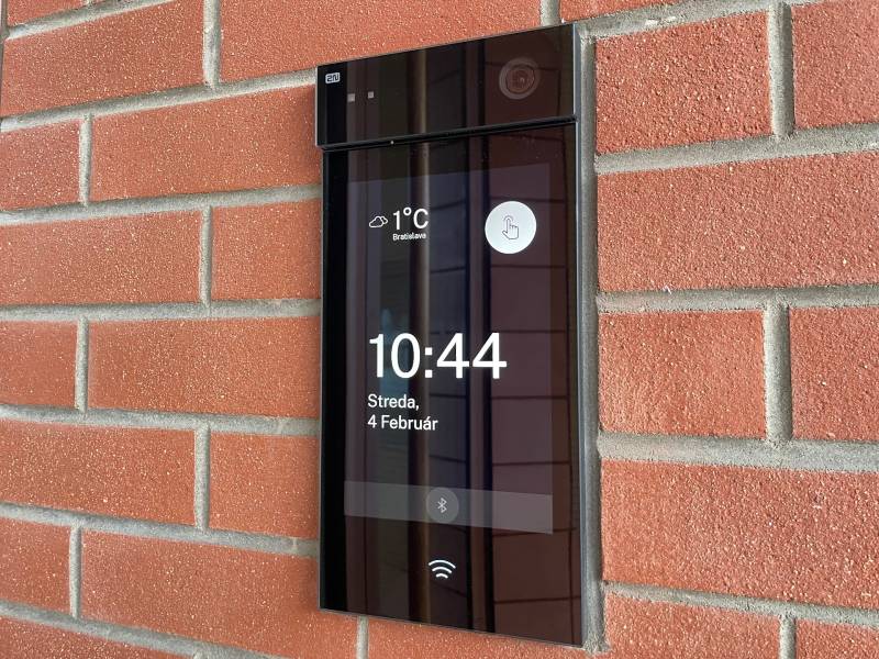 Digital doorbell on a brick wall, showing the time and temperature in Bratislava.