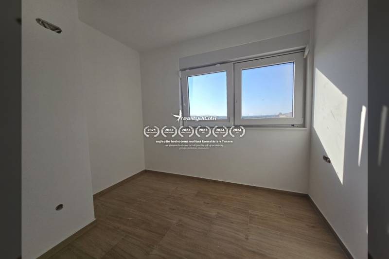 An empty room with wood-patterned flooring and two windows in a family house.